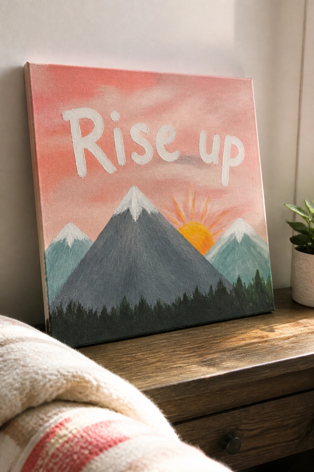 Canvas with 'Rise up' text above mountain landscape and rising sun on wood surface