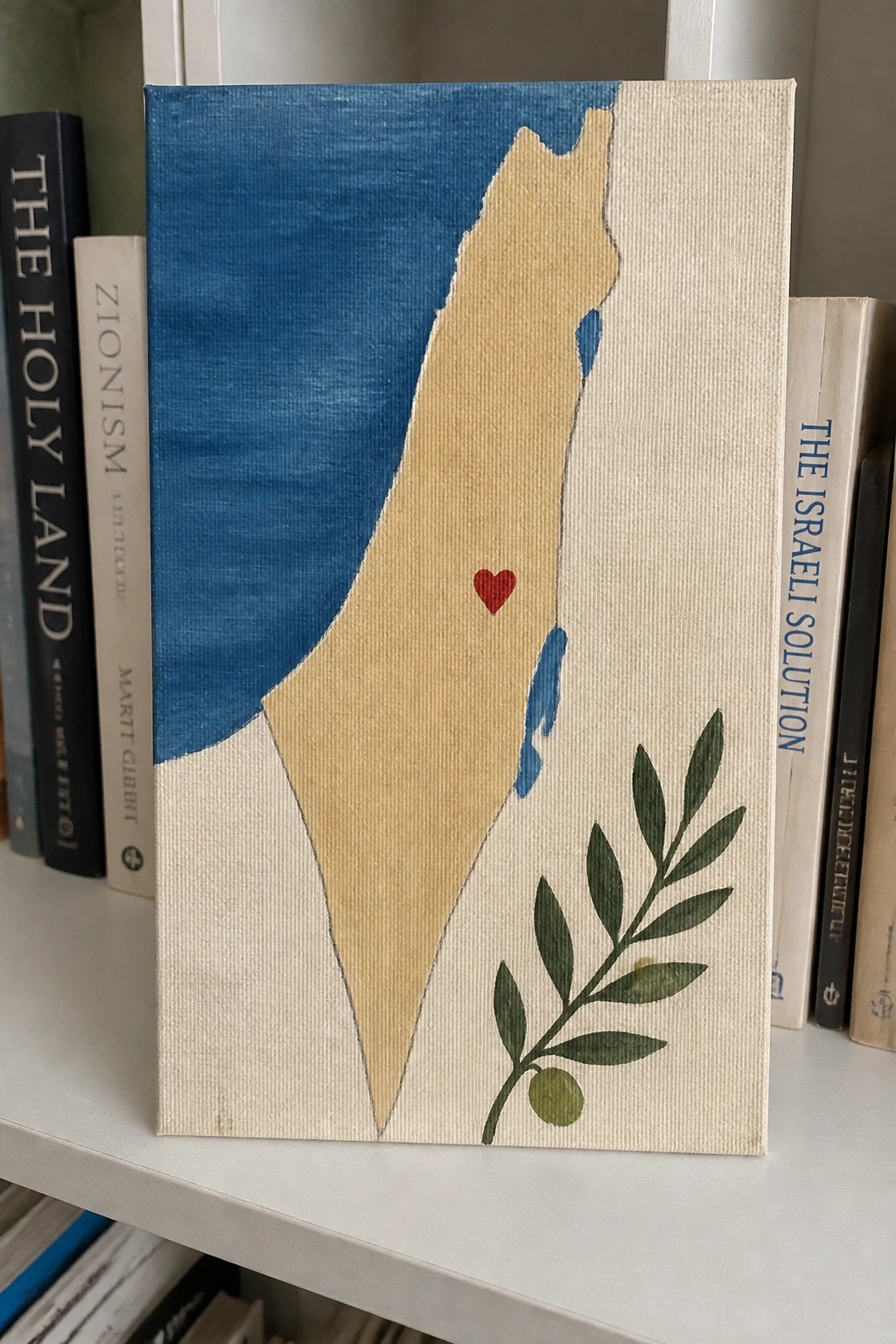 Painted canvas of Israel's beige outline with red heart and olive branch among books