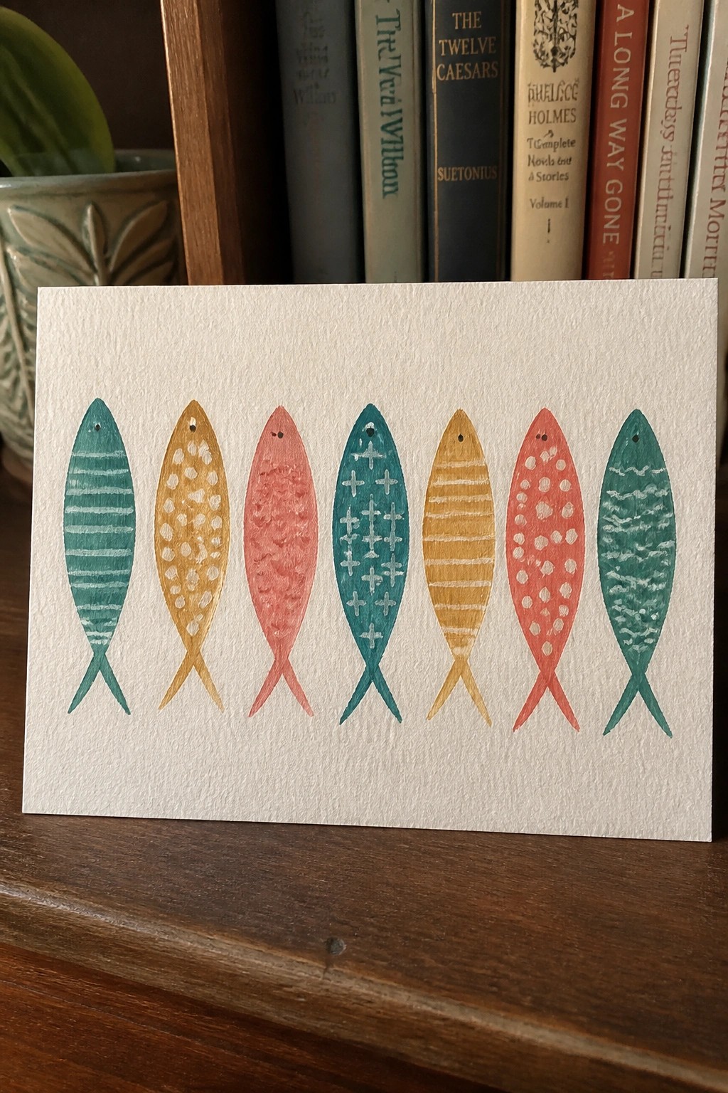 Seven fish with colorful patterns and textures lined up on white paper