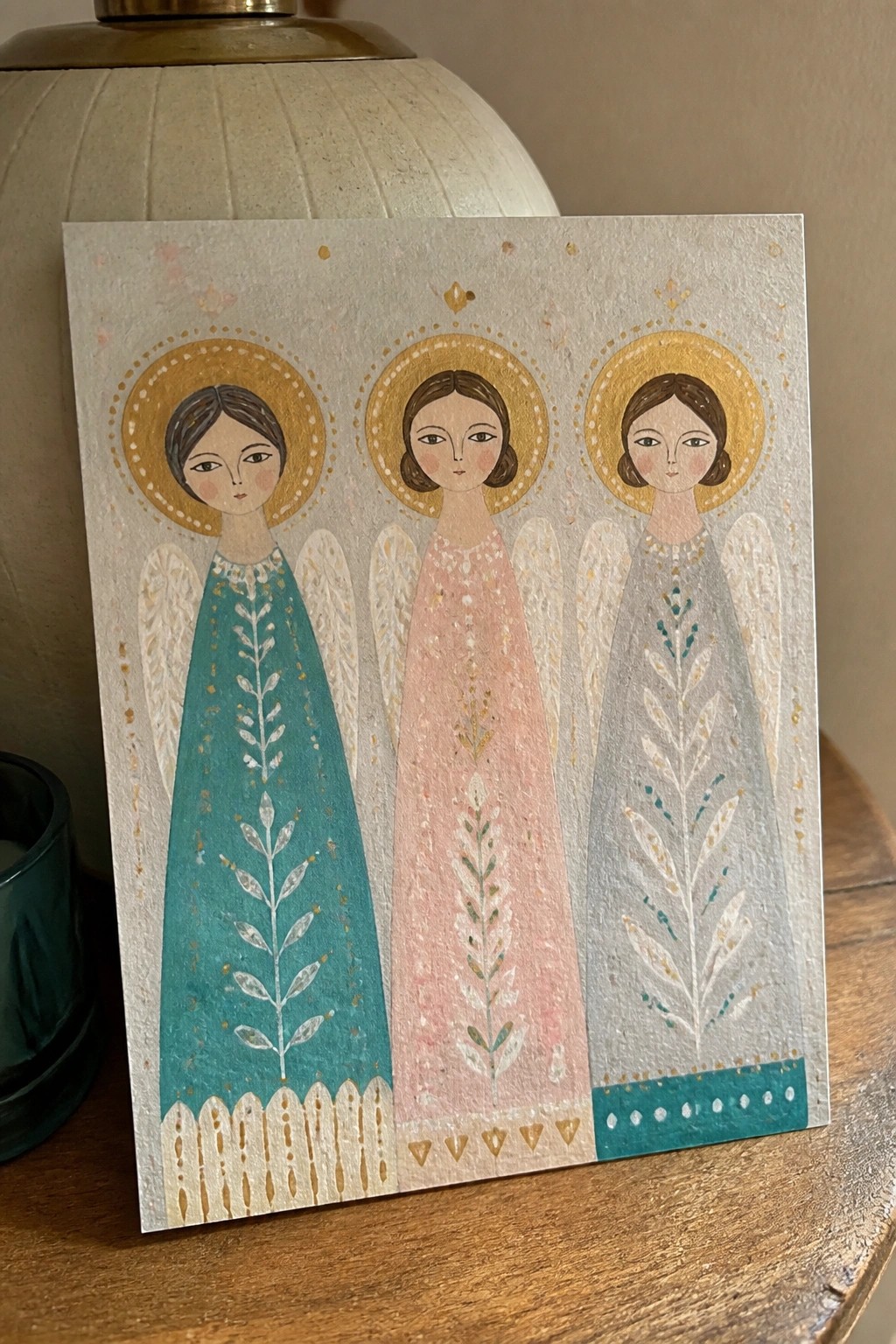 Three angels in teal, pink, and gray dresses with golden halos and wings