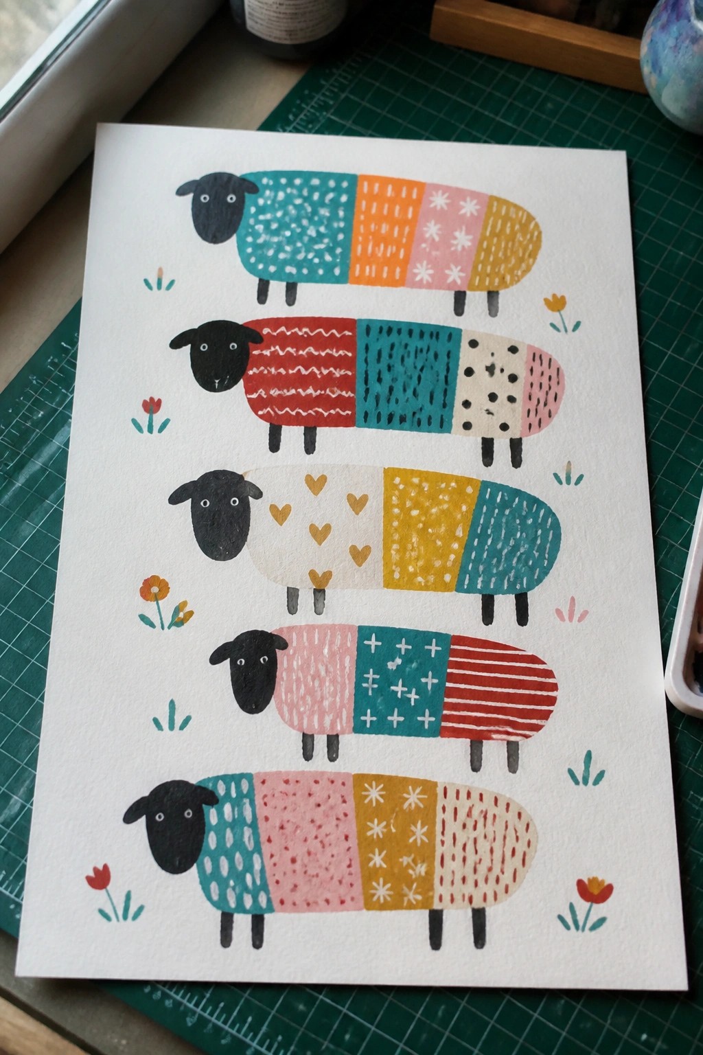 Five vertically stacked sheep with colorful patterned bodies amid small flowers on paper
