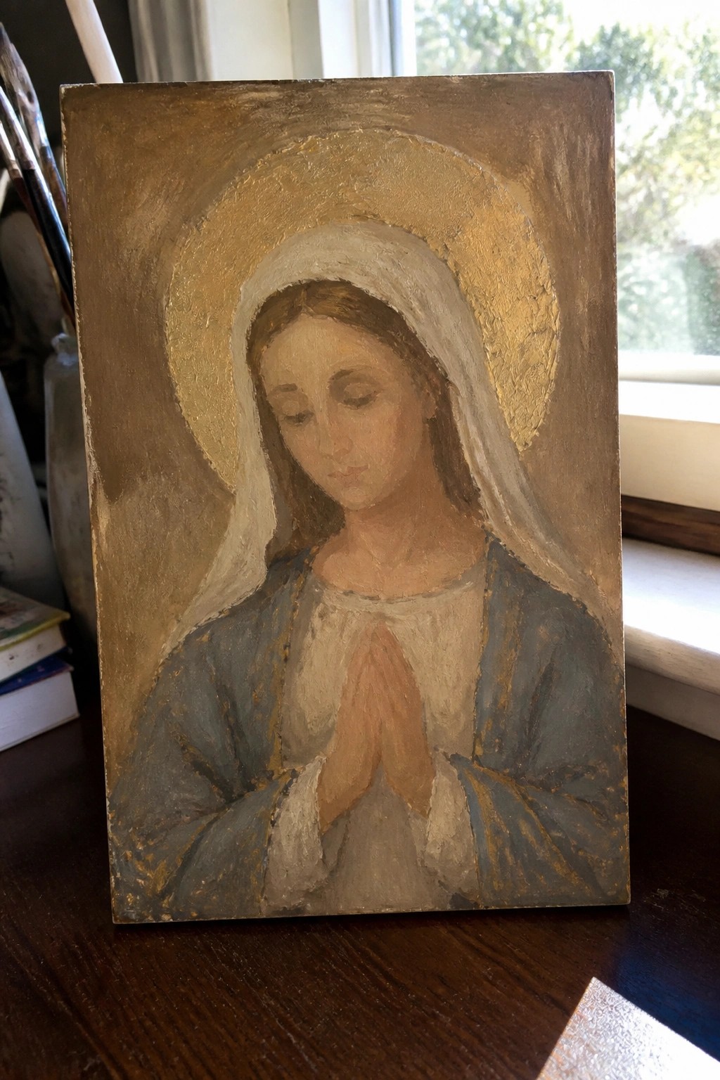 Oil painting of woman in blue robe and white veil with golden halo, hands in prayer.