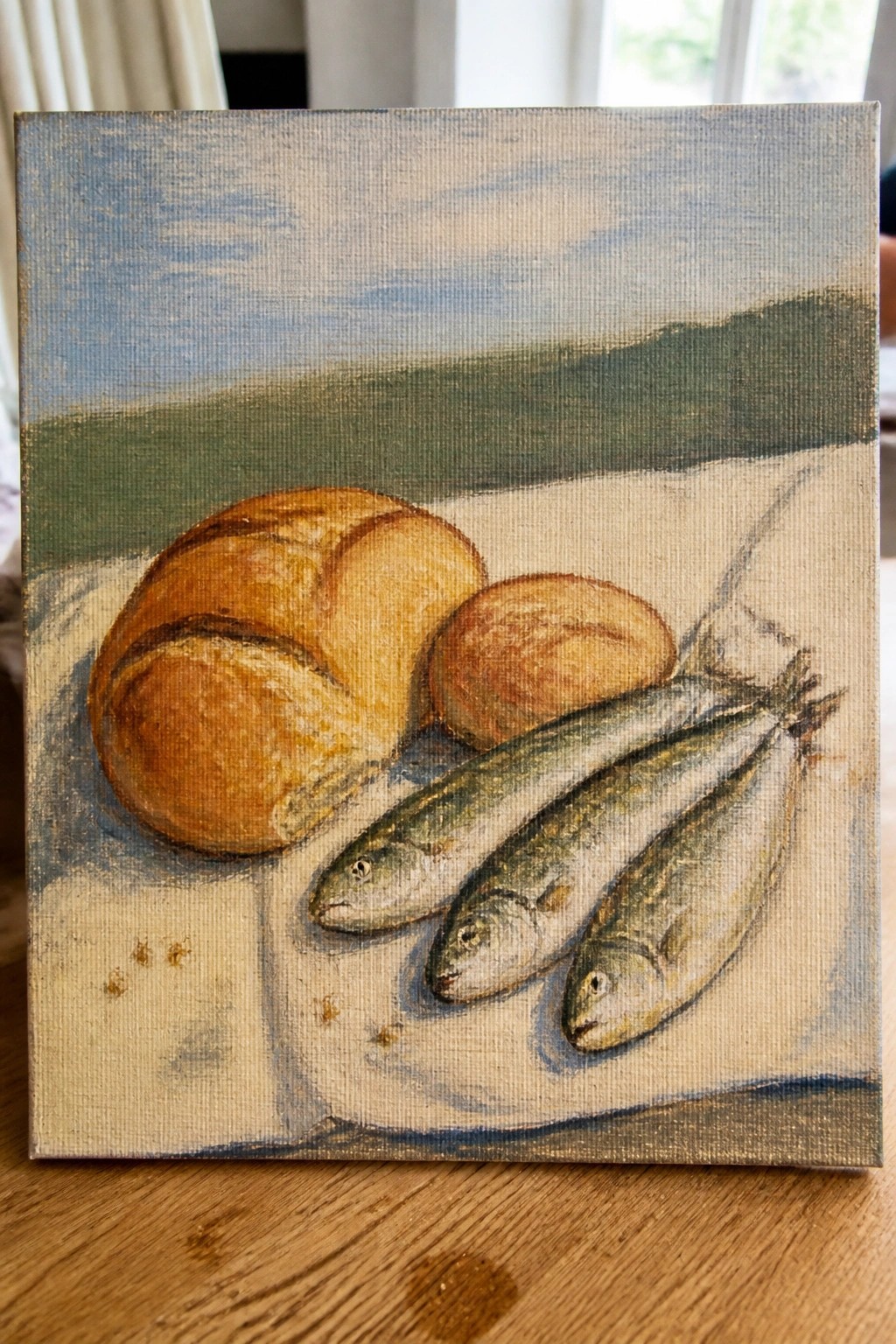 Two golden bread loaves and three fish on white cloth with blue backdrop