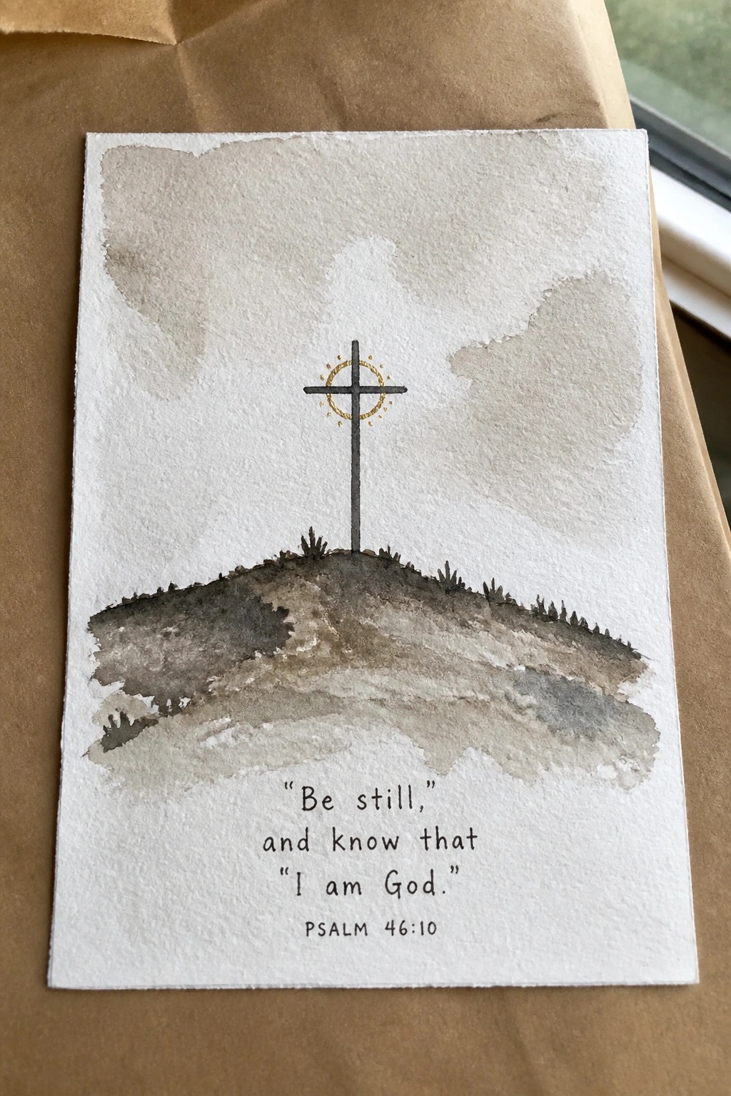 Watercolor of cross on hill with golden halo and Psalm 46:10 quote below.