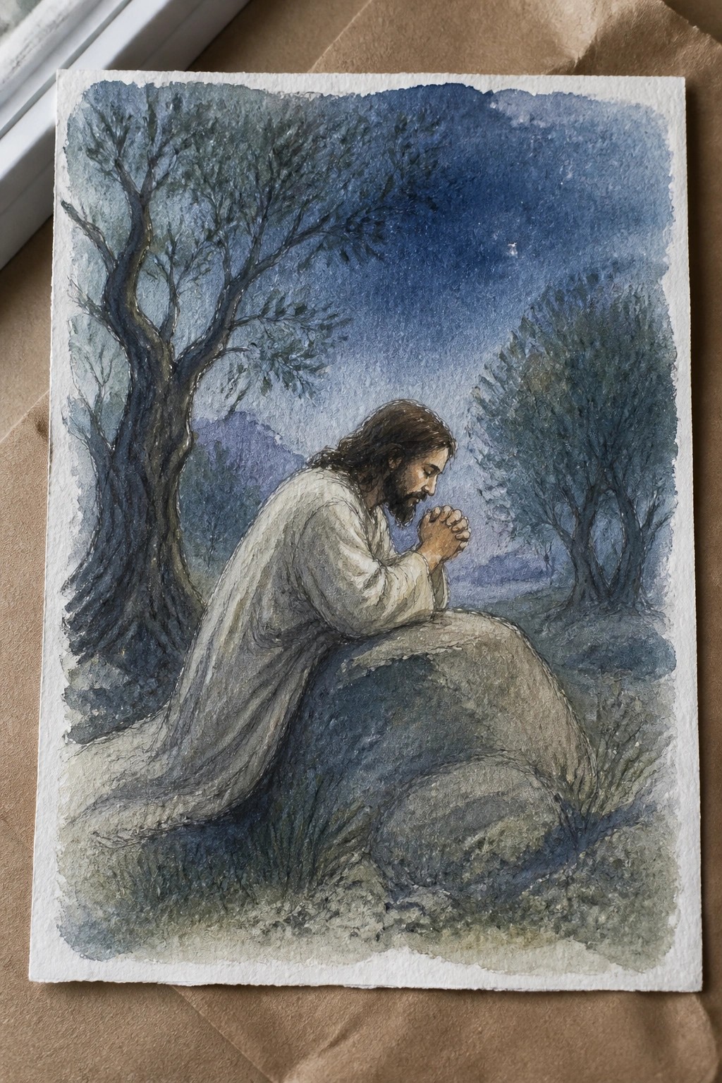 Watercolor of Jesus in white robes praying on a rock under starry night sky.