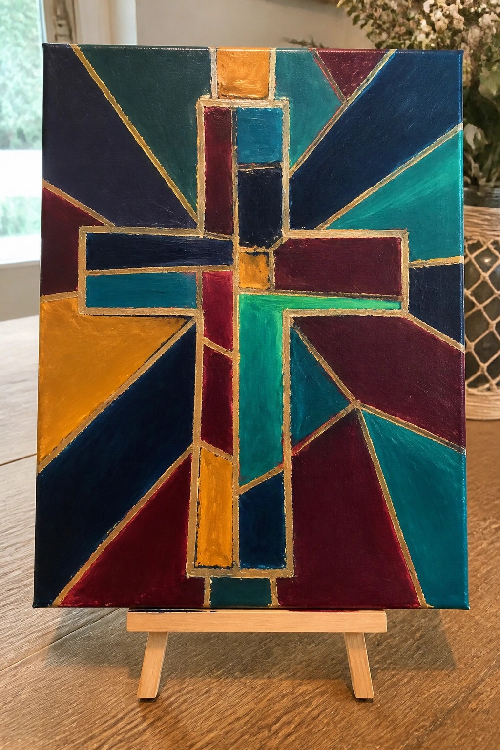 A painting of a cross made from colorful geometric shapes separated by gold lines on a canvas.