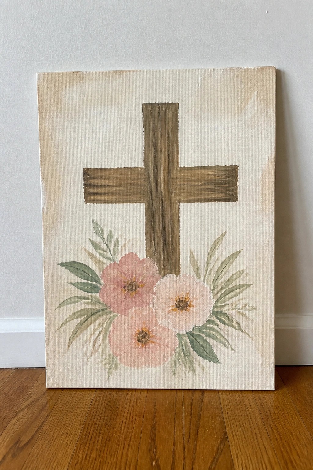 Wooden cross on beige canvas with pink flowers and green leaves at base