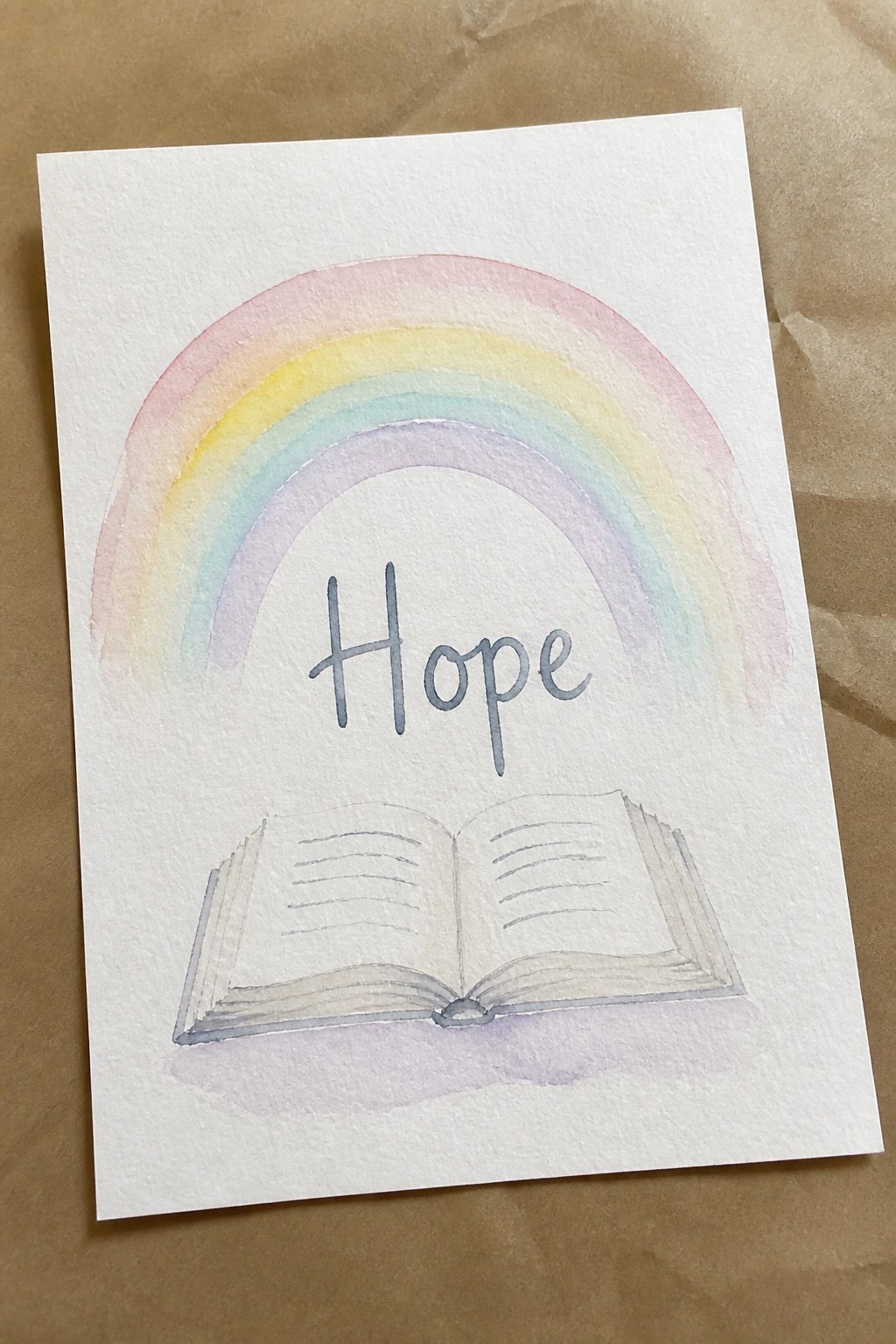 Watercolor rainbow above the word Hope and an open book on white paper