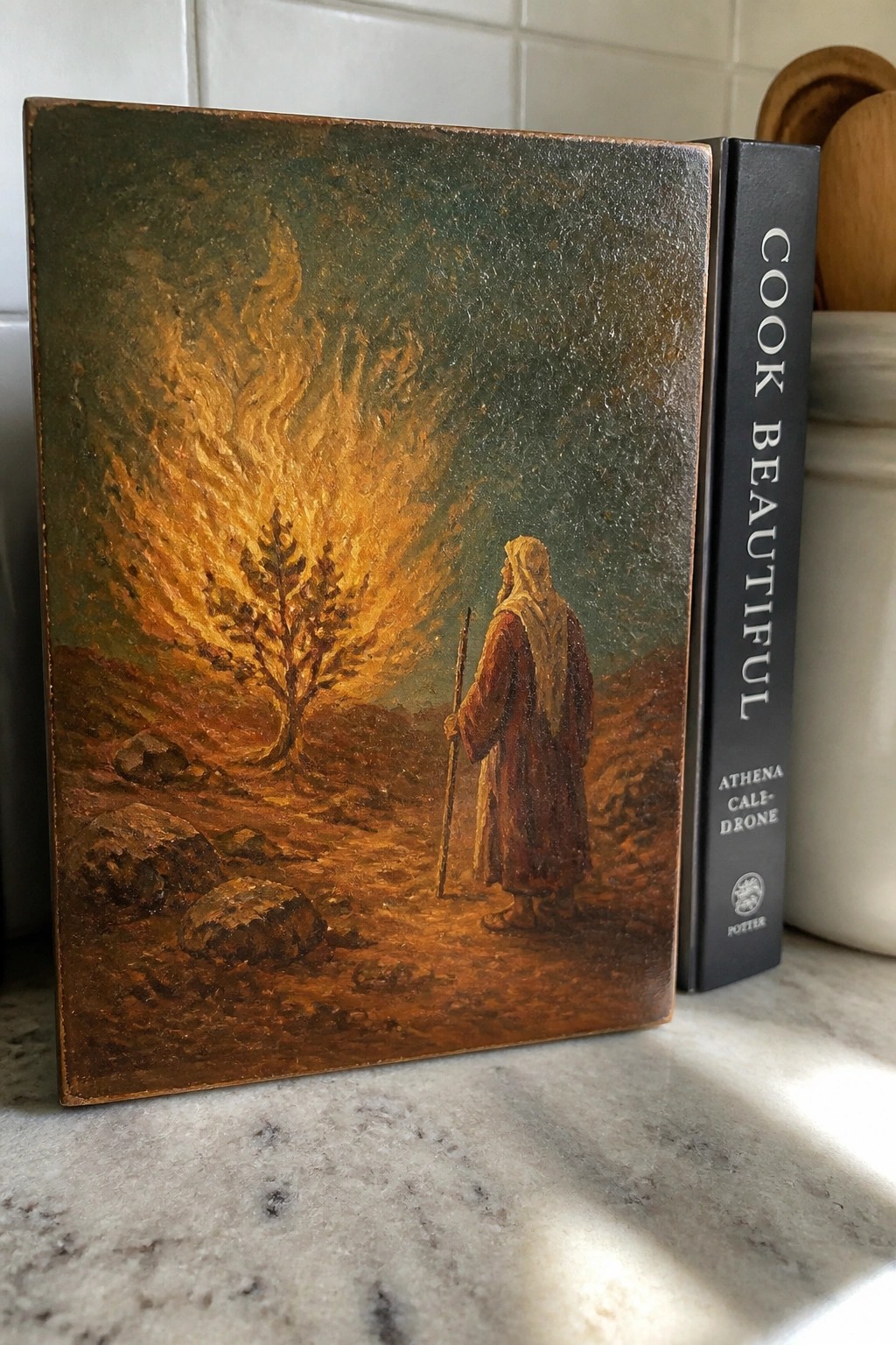 Worn book cover painting robed man with staff facing fiery burning bush beside cookbook spine