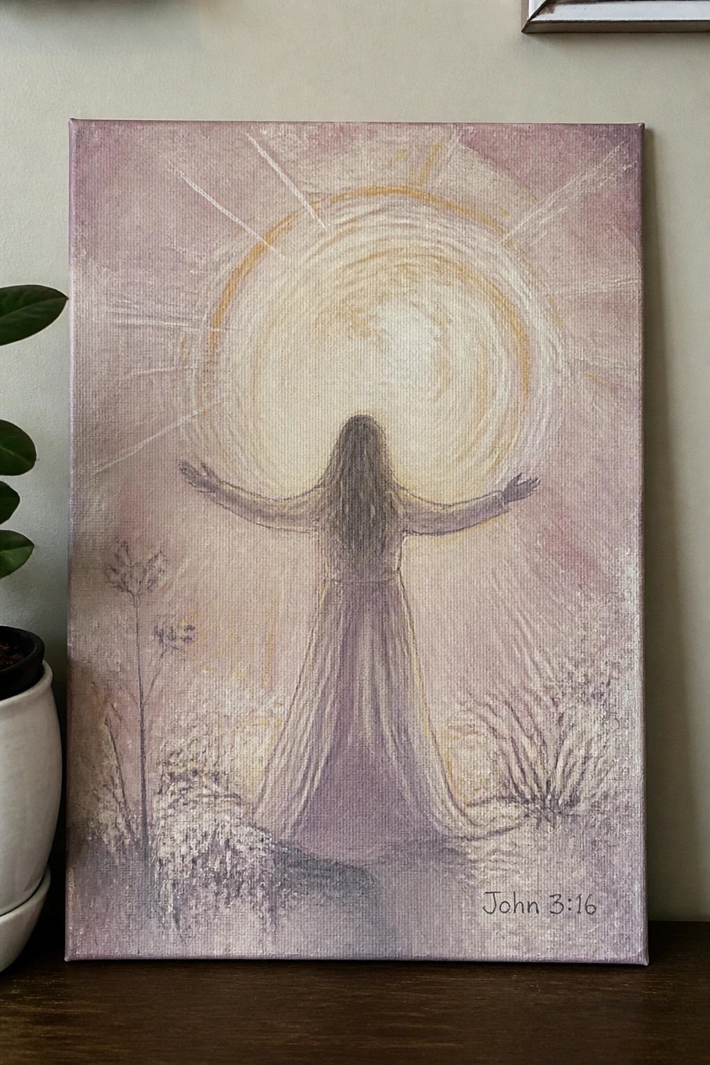 Canvas painting of a woman with outstretched arms facing a glowing sun, with John 3:16.