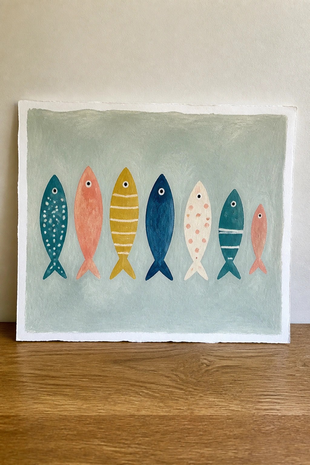 Seven colorful fish painted in a row on pale green background
