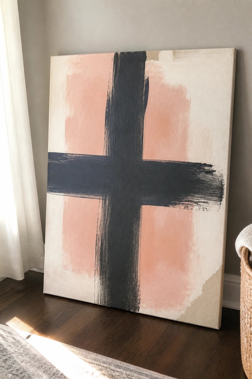 Abstract painting with bold black cross on soft pink and beige canvas leaning against wall