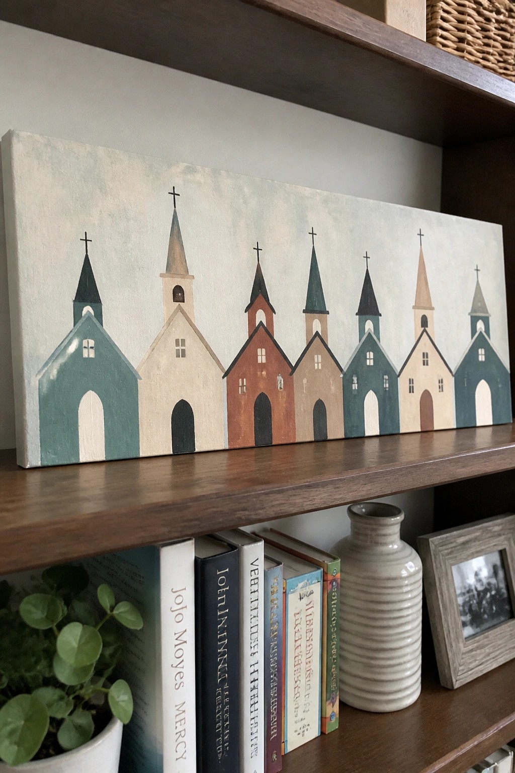 Row of seven pastel churches with steeples on canvas above books on shelf