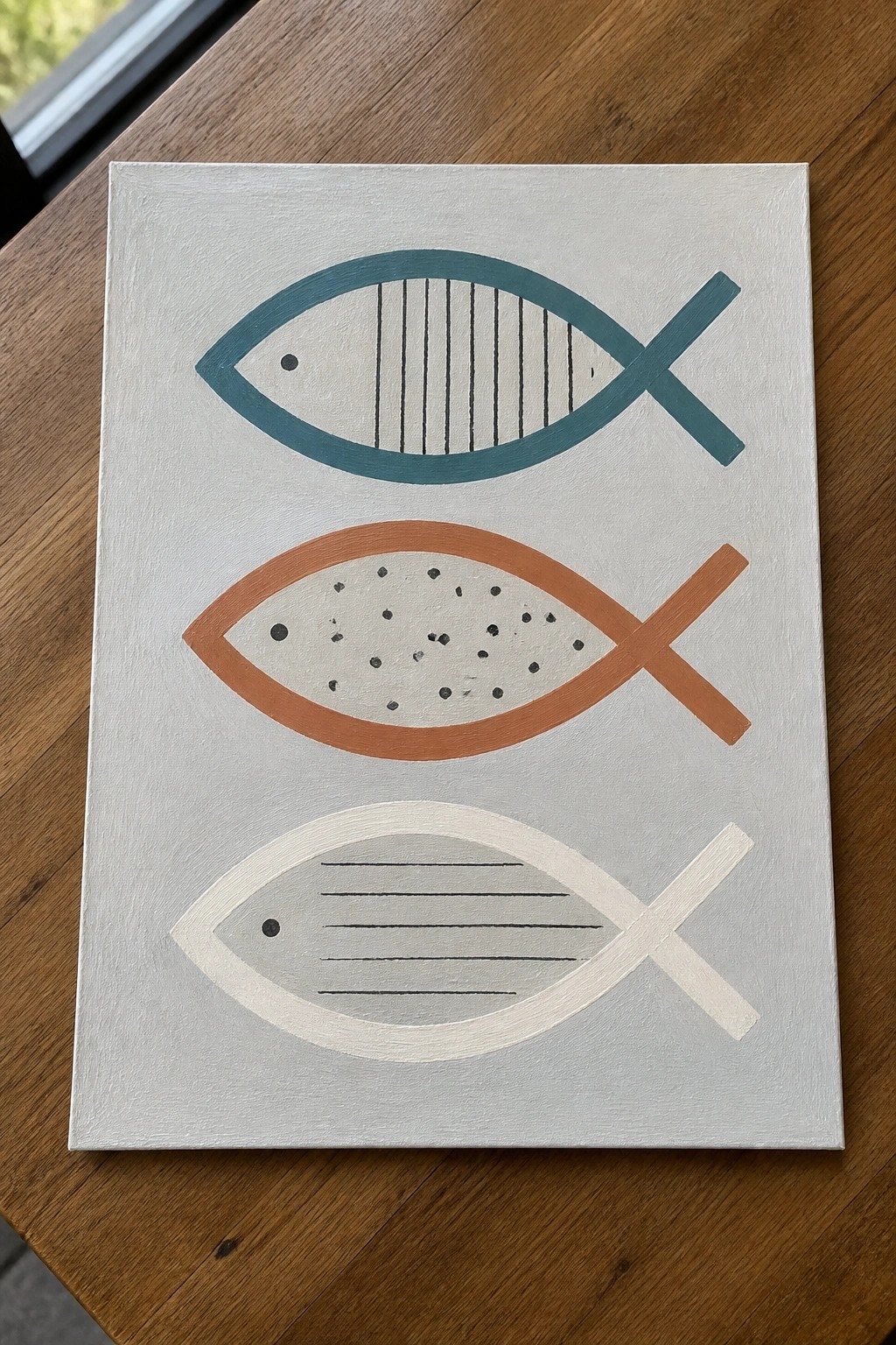 Three fish symbols painted on canvas in teal, orange, and white.