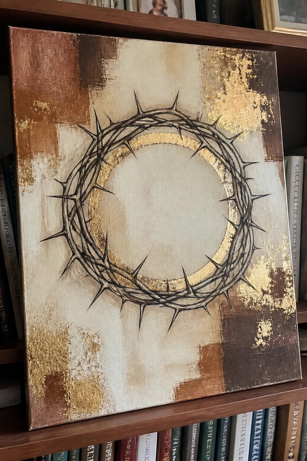Crown of thorns with gold halo on abstract brown and beige canvas atop bookshelf.