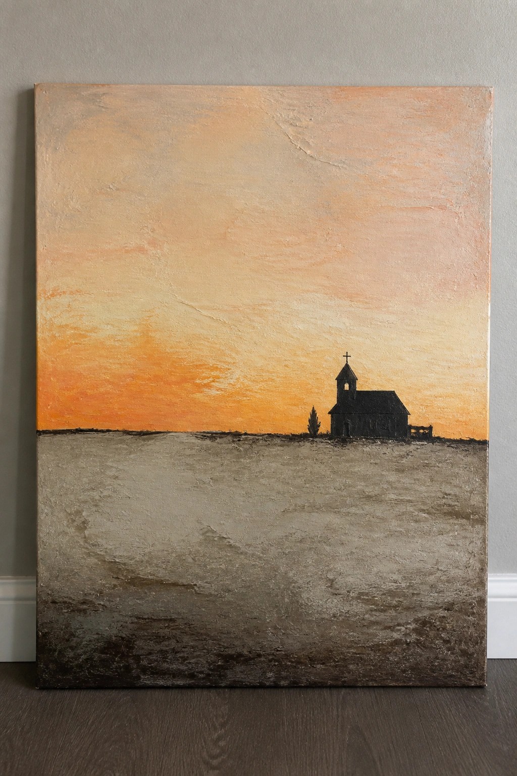 Silhouetted church with cross against vibrant orange sunset over textured barren field.