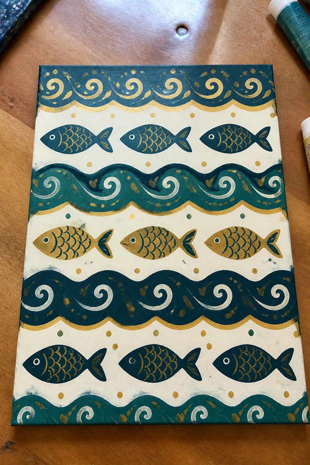 Hand-painted canvas with rows of teal and gold fish amid swirling wave patterns.