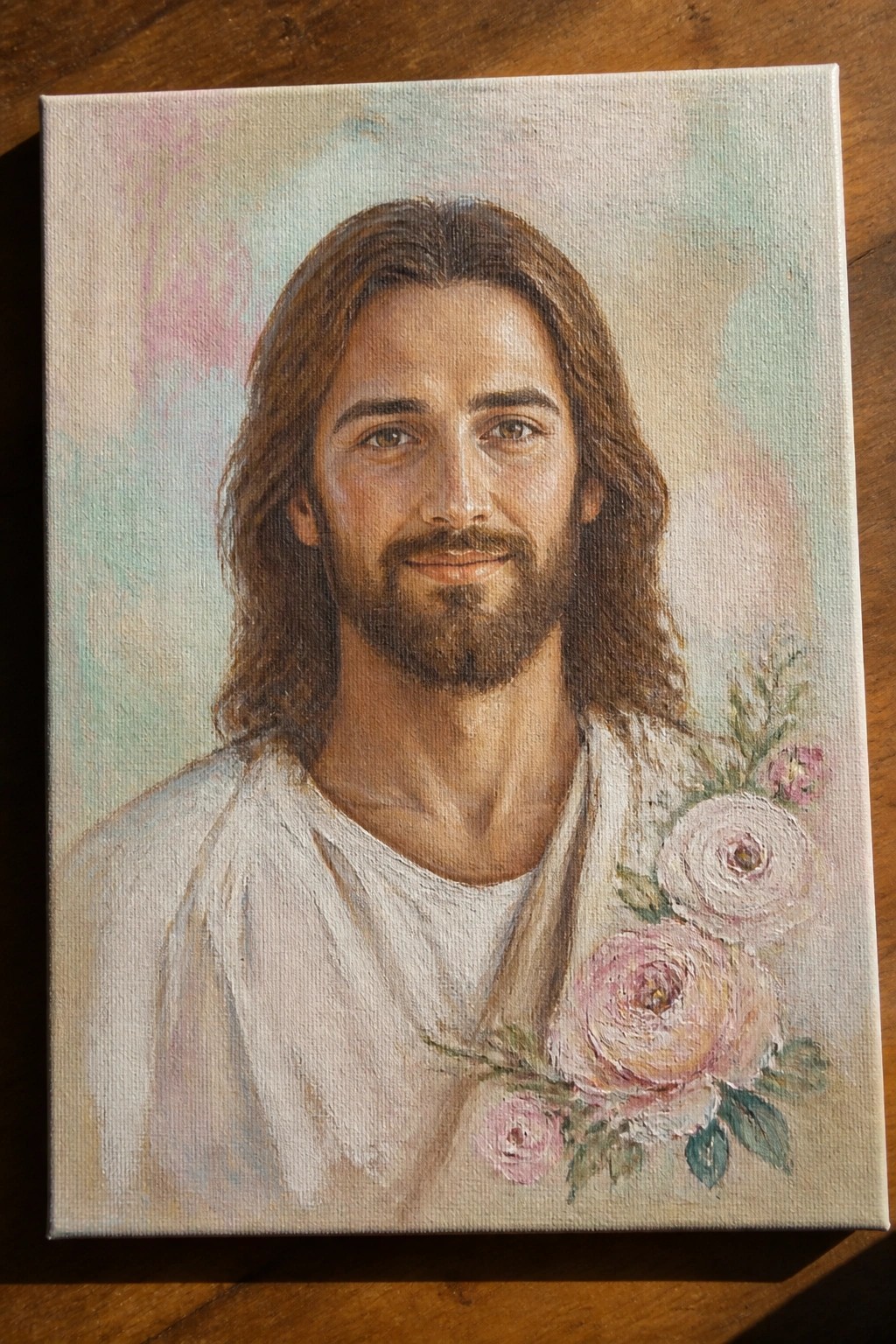 Oil painting of Jesus with long hair, beard, white robe, and pink roses on canvas
