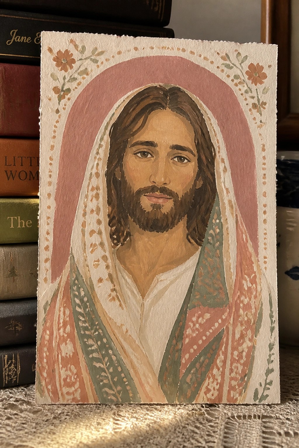 Watercolor of Jesus with beard in patterned robes against pink floral arch beside books.