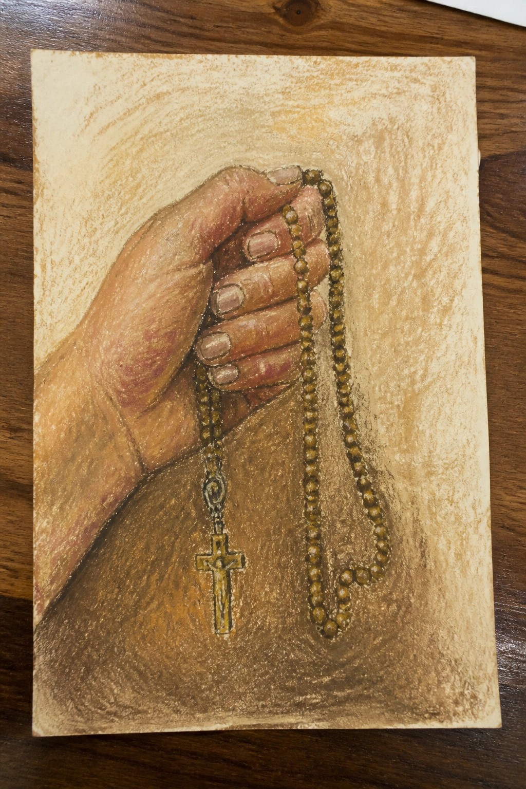 Realistic colored pencil drawing of hand holding brown rosary beads with crucifix
