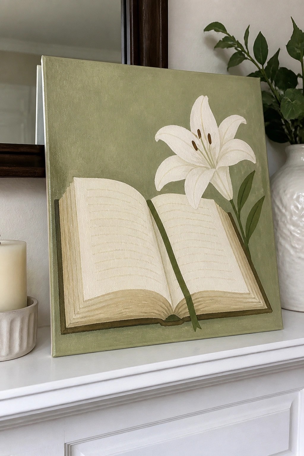 Sage green painting of open book with white lily on white mantel with candle and vase
