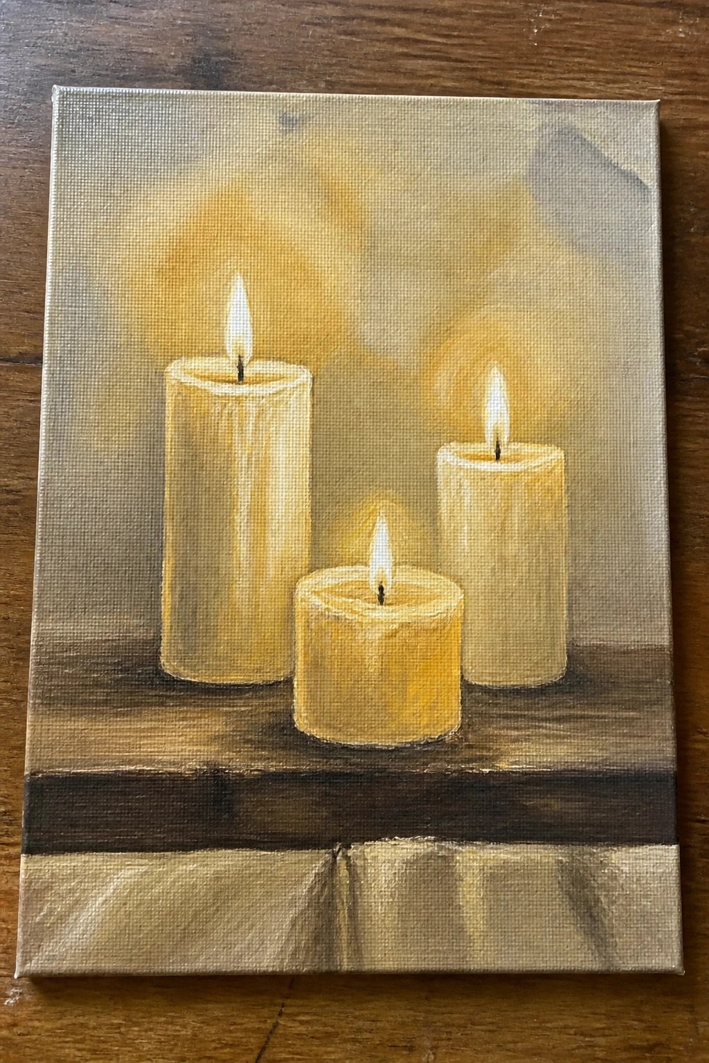 Three lit yellow candles glowing on a dark wooden surface in soft light