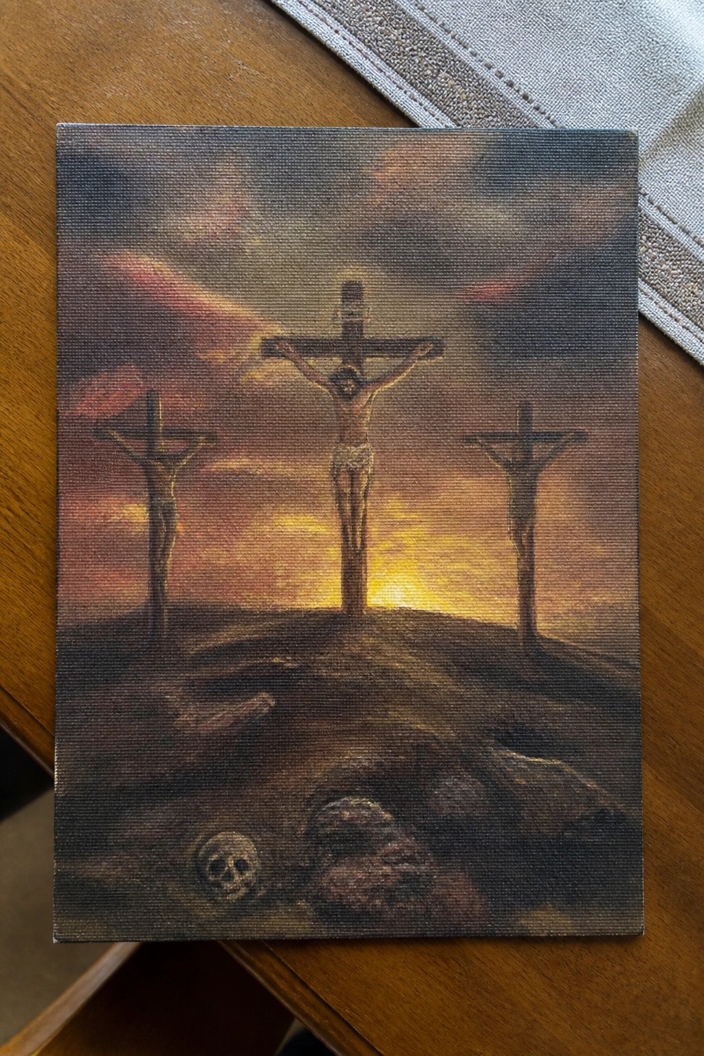 Three crucified figures on crosses at sunset on rocky hill with skull in foreground.