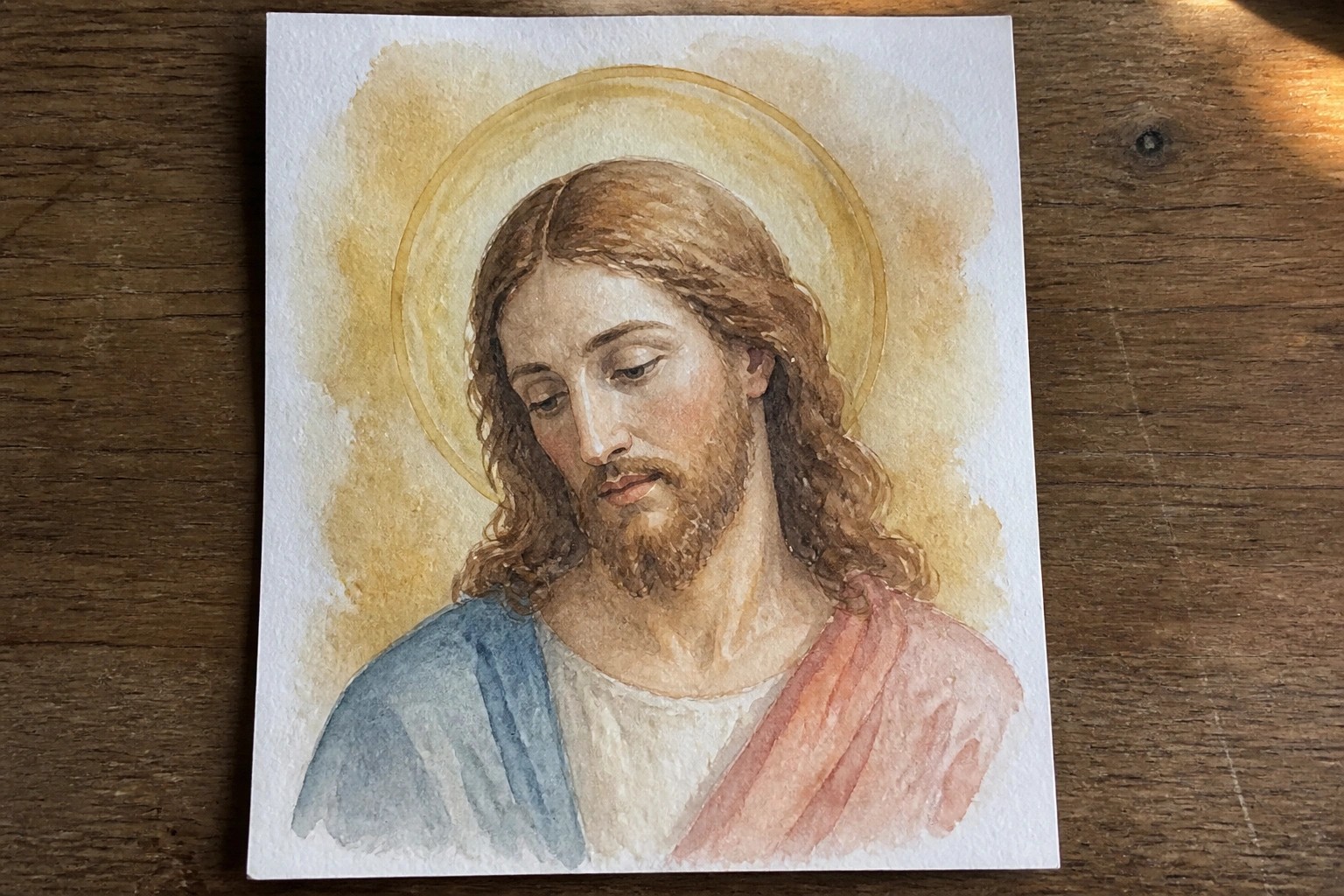Watercolor portrait of Jesus with long brown hair, beard, golden halo, and red-blue robes.