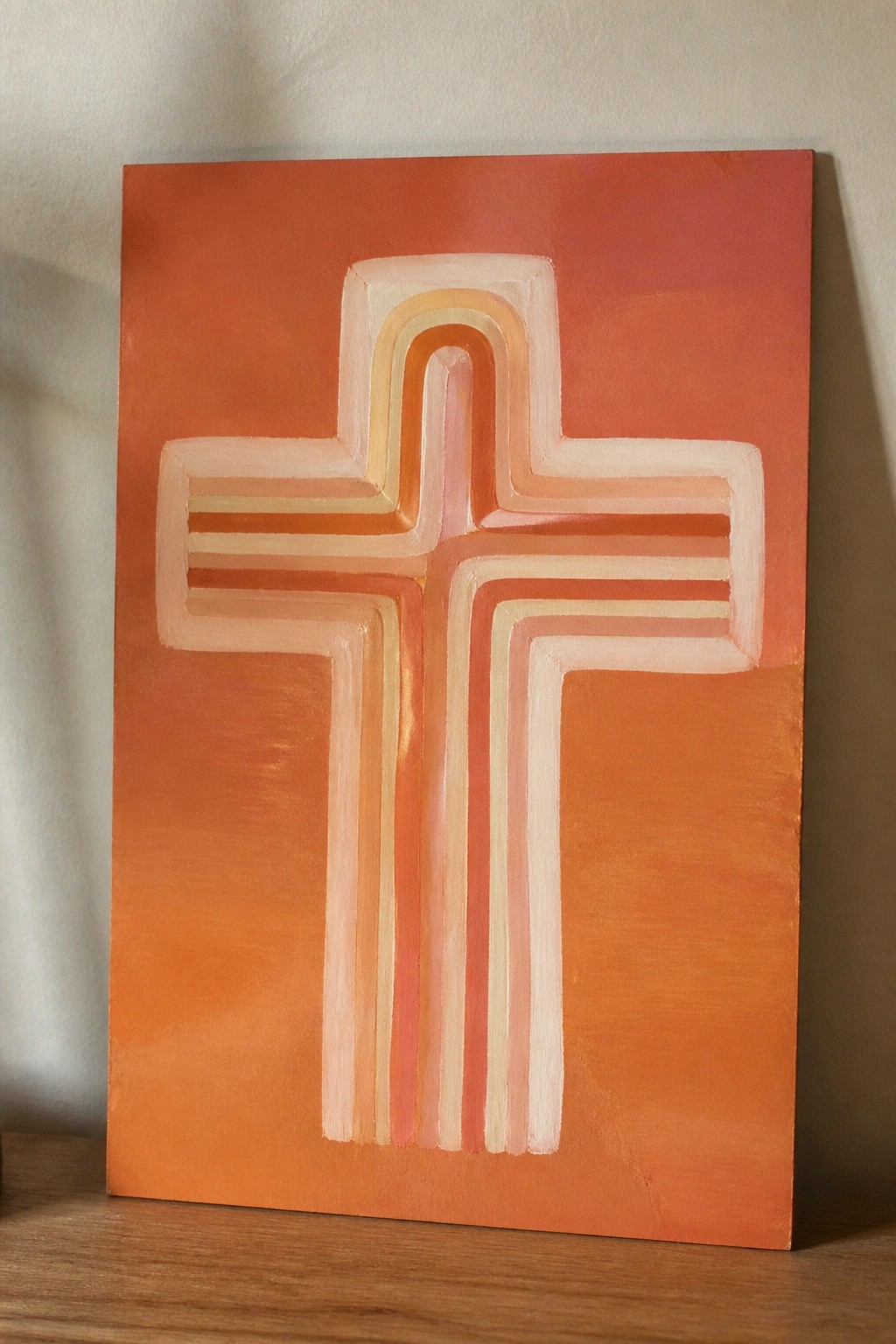 Orange canvas with layered cross in peach, pink, and white stripes.