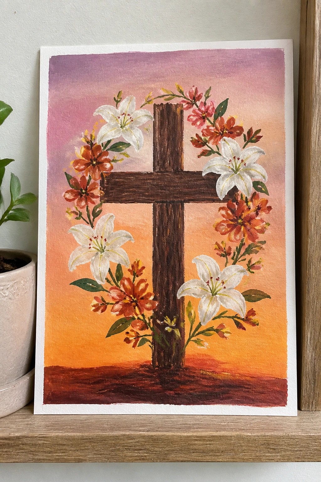 Watercolor of wooden cross with white lilies and orange flowers on sunset gradient.