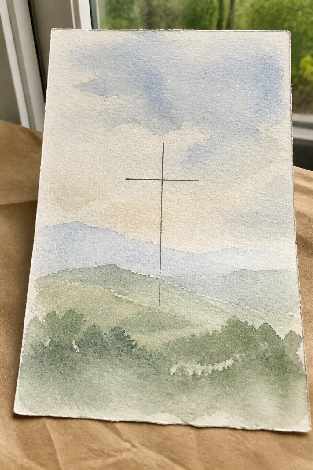 Watercolor landscape of green hills under blue sky with centered black cross