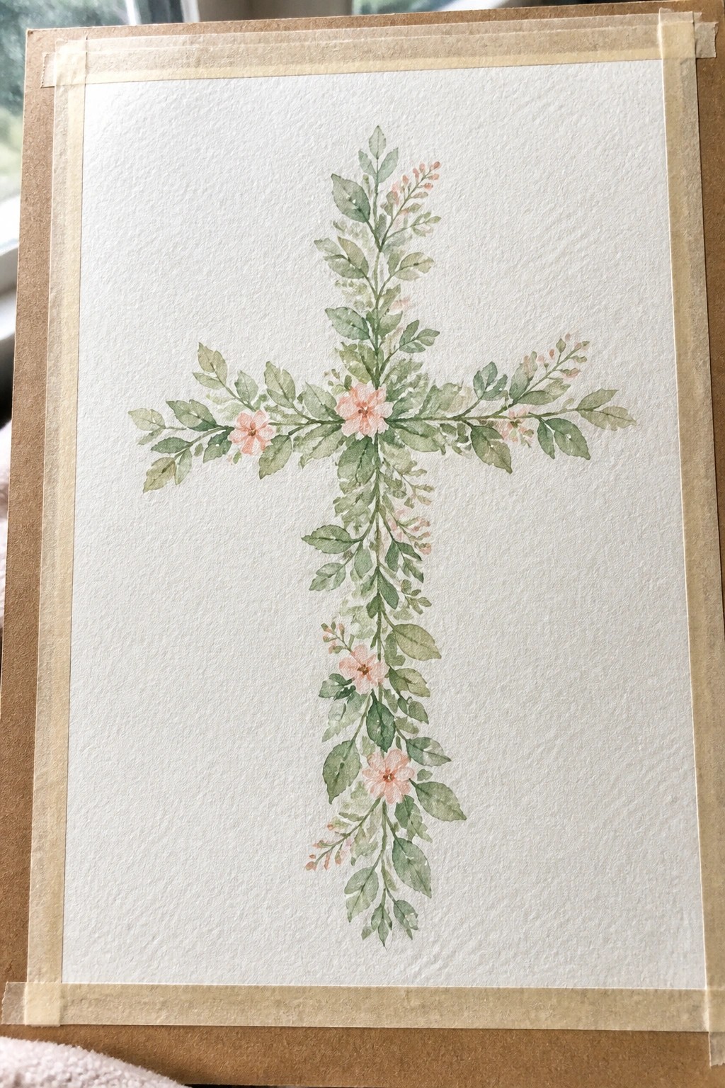 A watercolor painting of a cross made from green leaves and pink flowers taped onto brown paper.