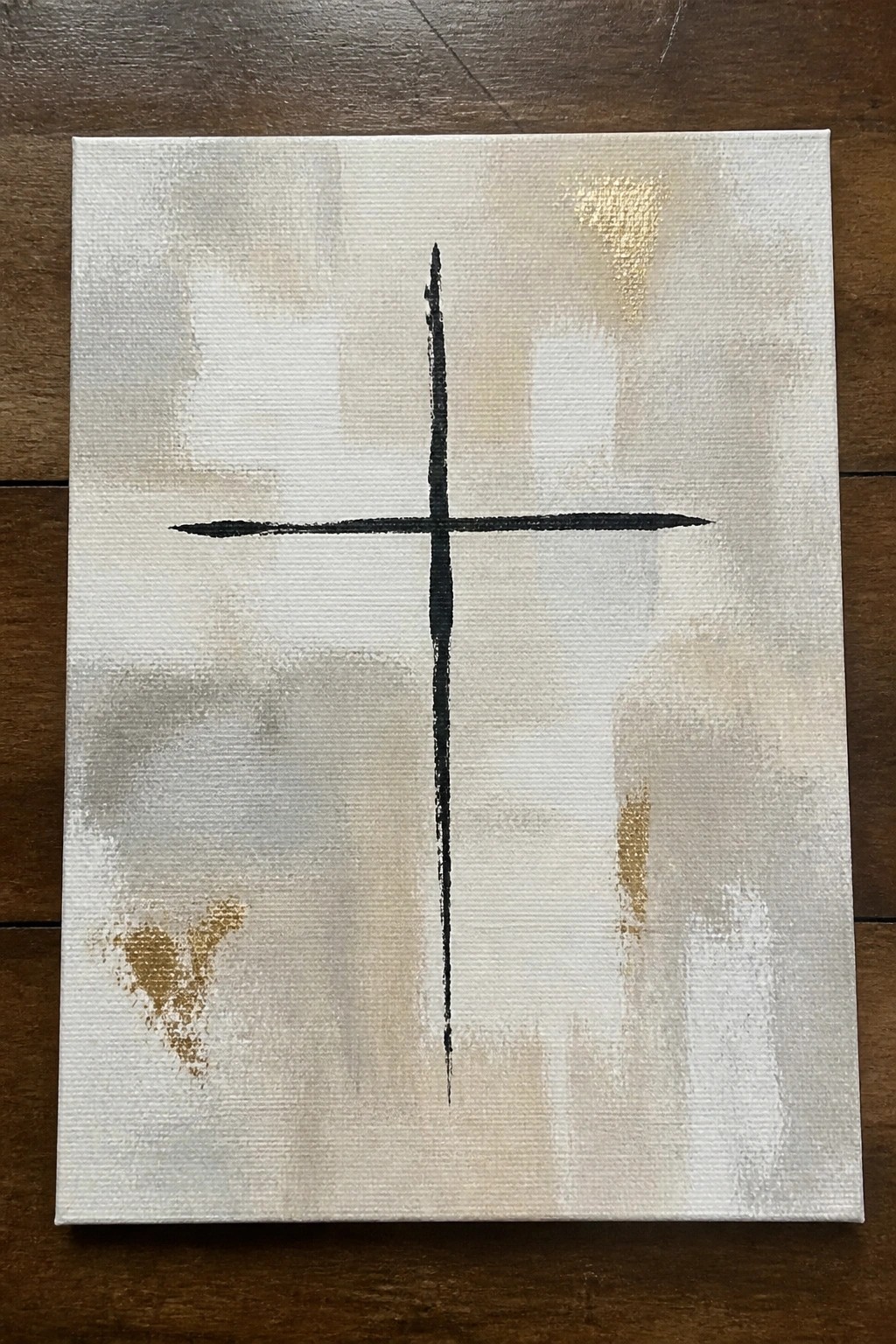Abstract painting of bold black cross on beige, white, and gold textured canvas.