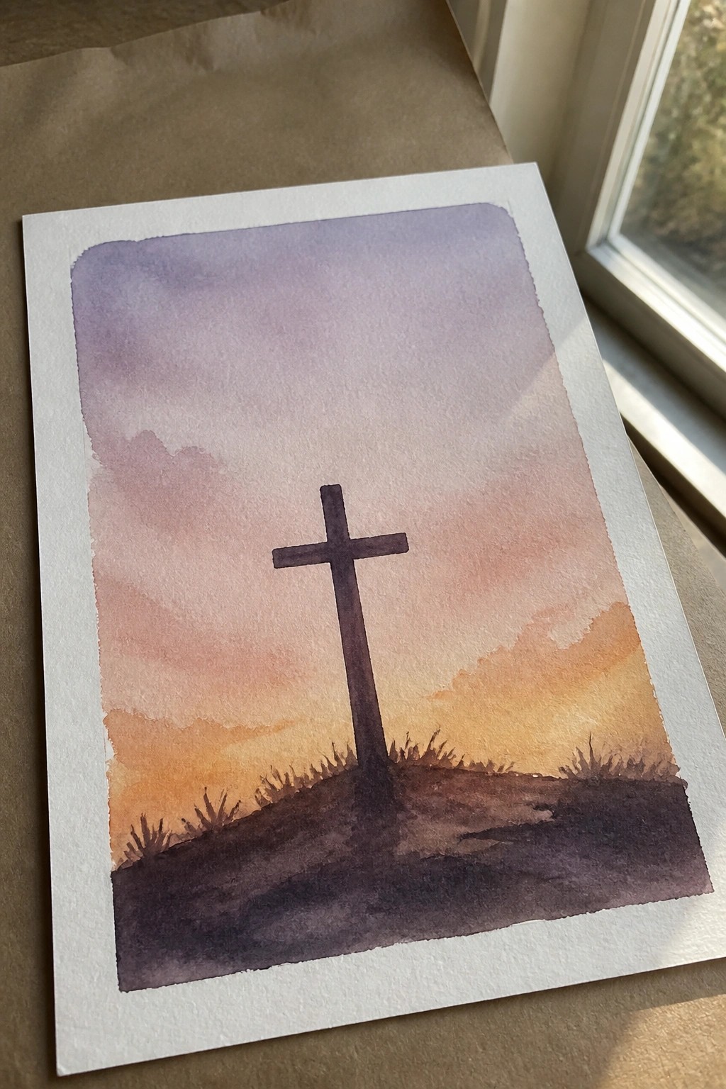 Watercolor painting of a cross on a hill under a purple-orange sunset sky