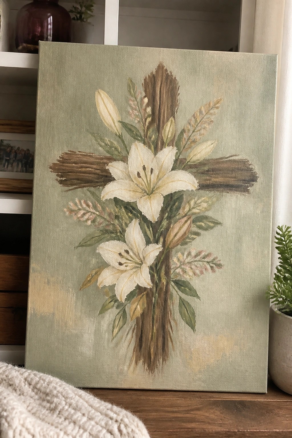 Canvas painting of white lilies around wooden cross with green foliage on sage background.