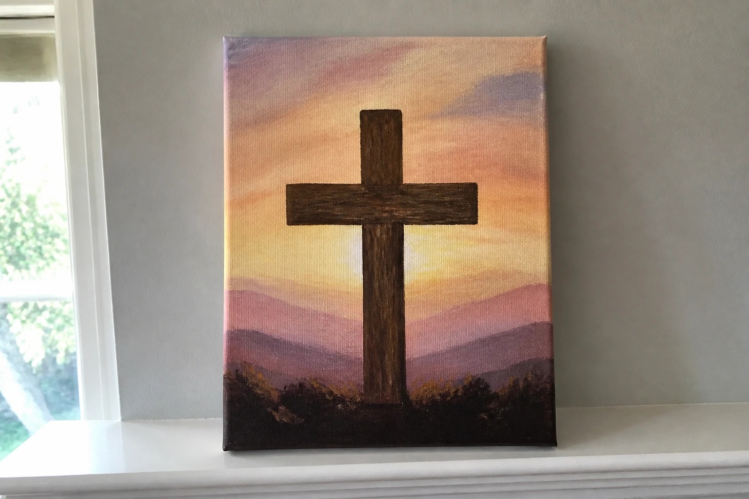 Brown wooden cross against vibrant orange-pink-purple sunset sky over layered mountains
