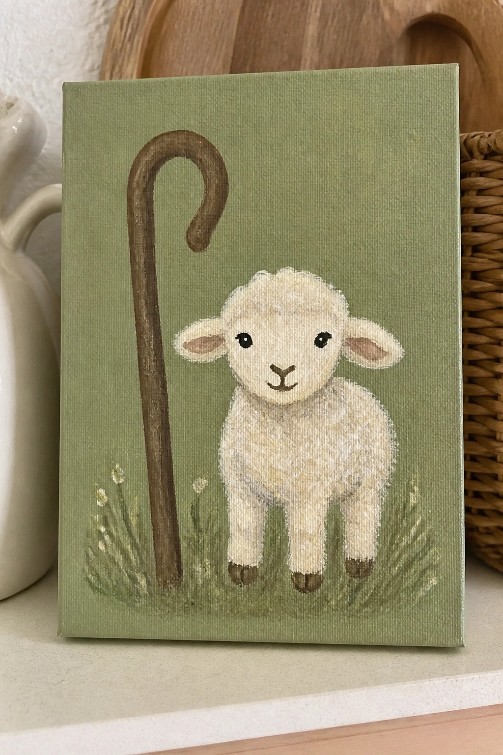 Cute white lamb beside brown shepherd's crook on green canvas with grass and flowers