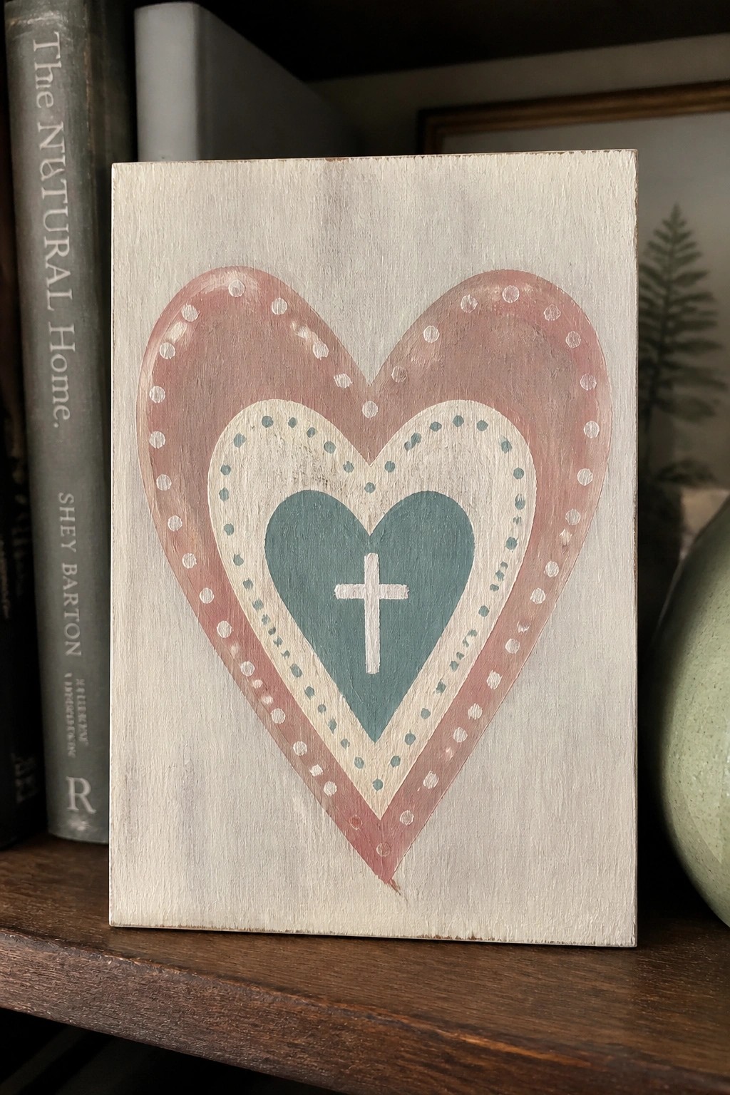 Wooden plaque with concentric pink, cream, and teal hearts and white cross