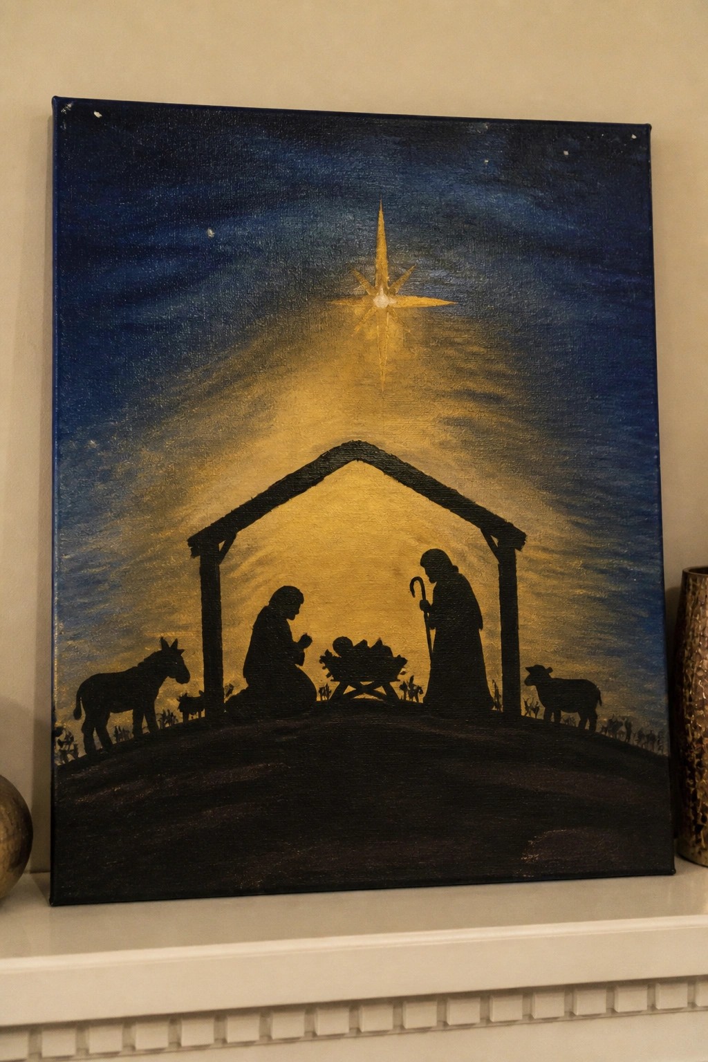 Silhouetted nativity with Mary, Joseph, manger, donkey and sheep under glowing star.