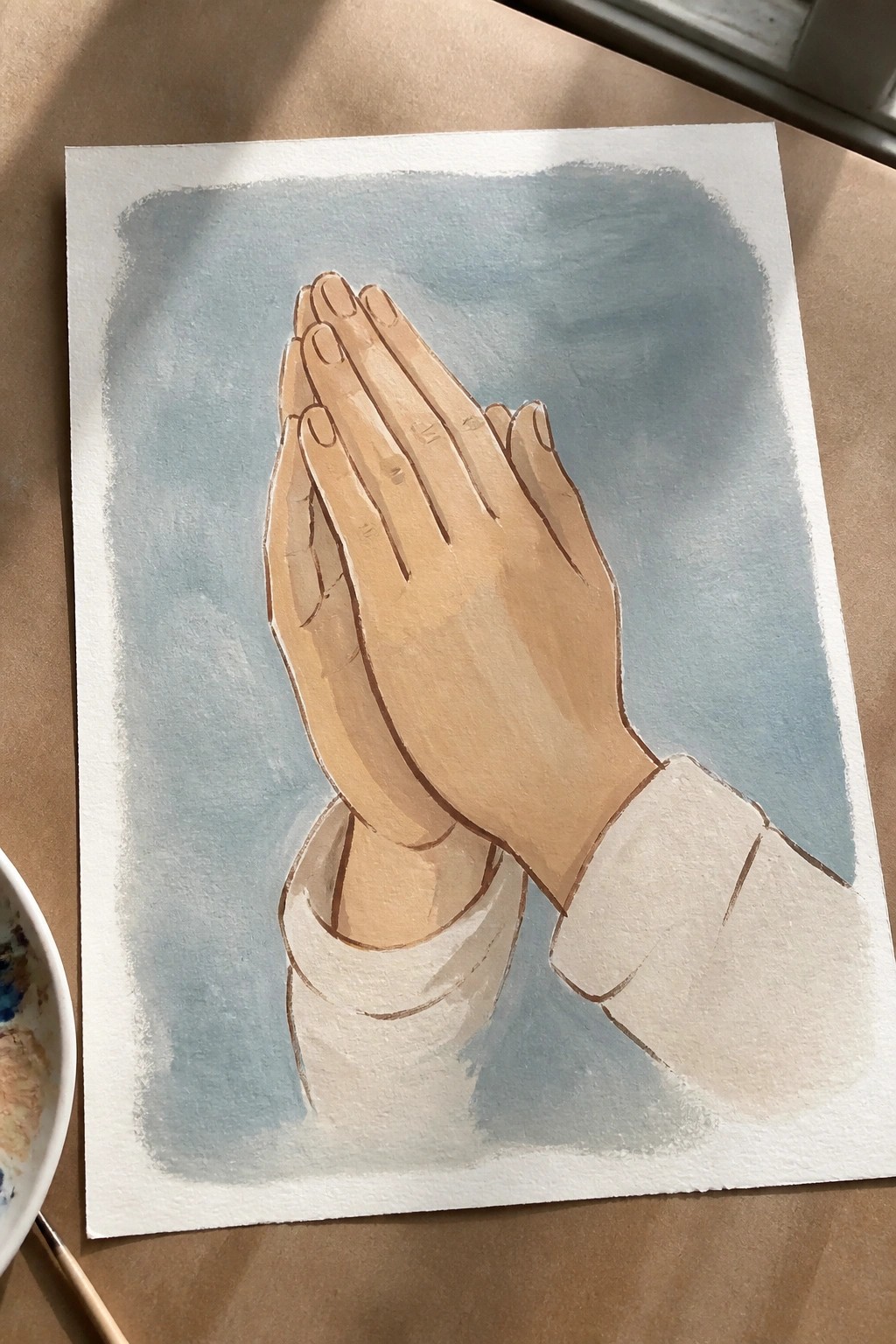Watercolor painting of praying hands with white sleeves against blue wash background