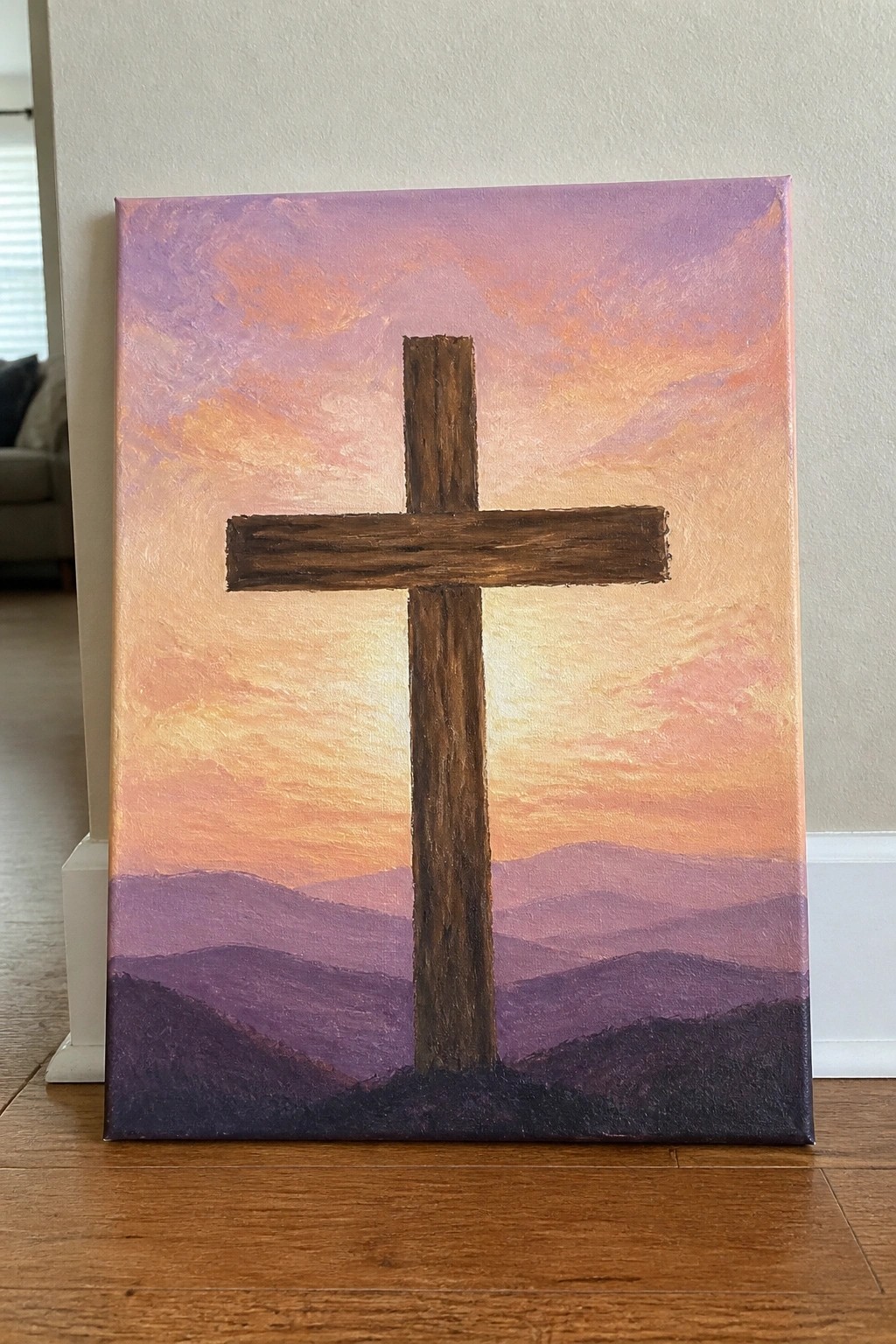 Brown wooden cross against vibrant orange-pink-purple sunset sky over layered mountains