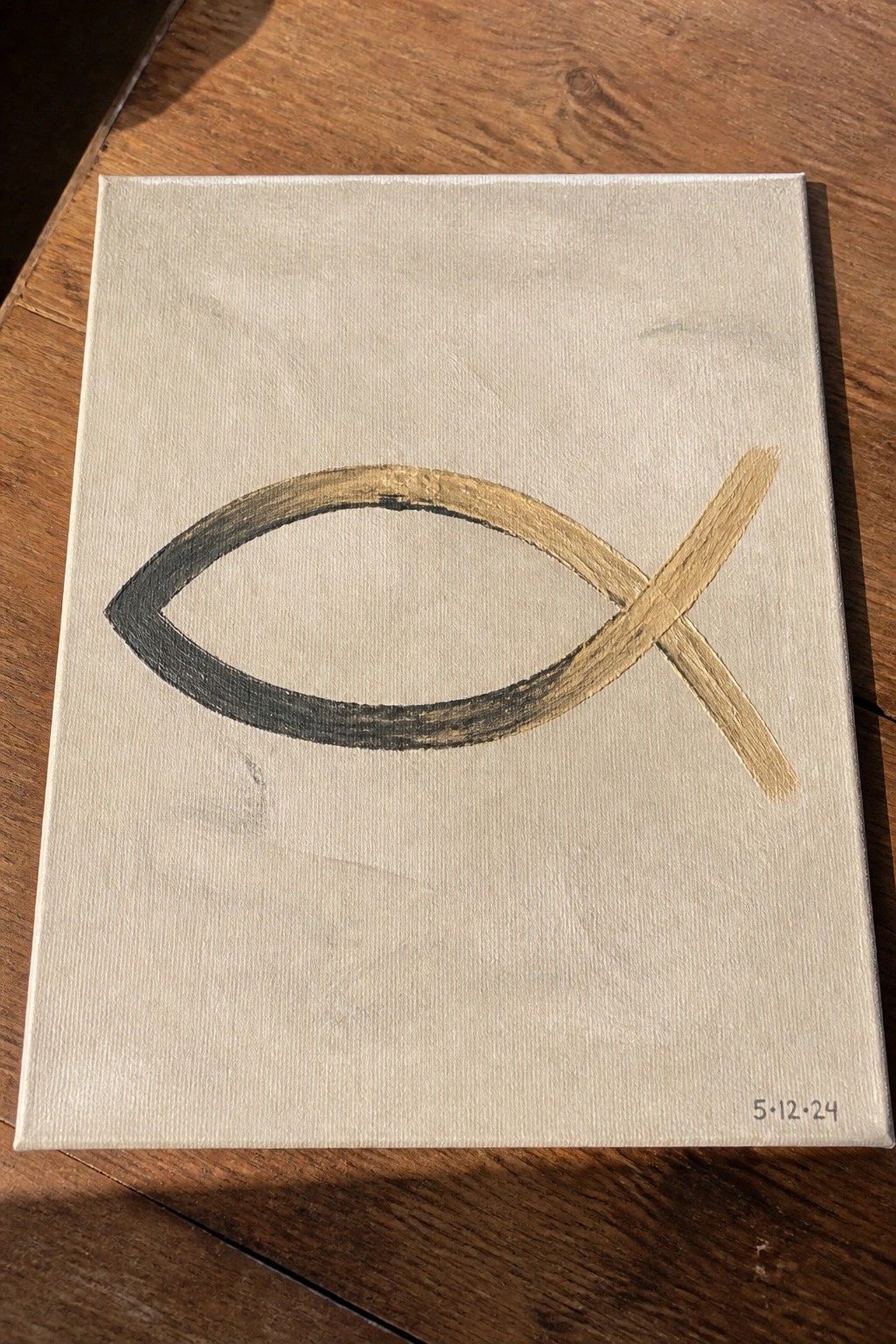 Beige canvas with black and gold ichthys fish symbol on wood