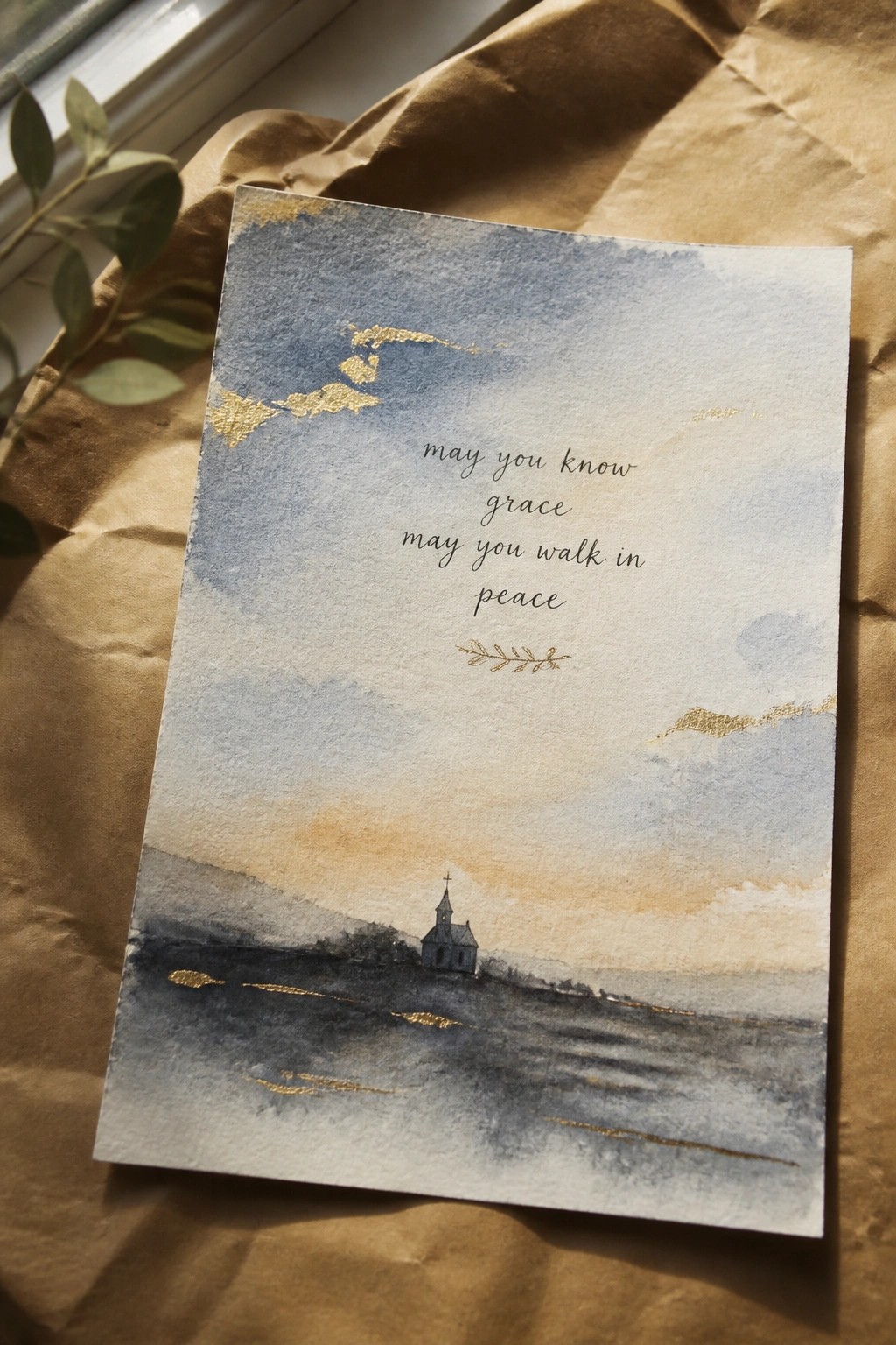 Watercolor card with church by water, blue-orange sky, gold text and accents on brown paper.