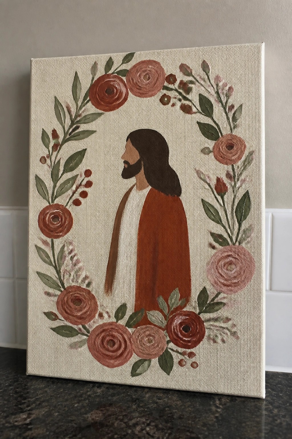 Jesus in profile with long hair and beard, wearing brown robe inside floral wreath.