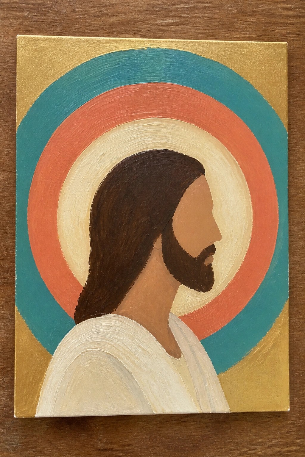 Profile of Jesus with long brown hair, beard, white robe, and vibrant concentric halo on gold.