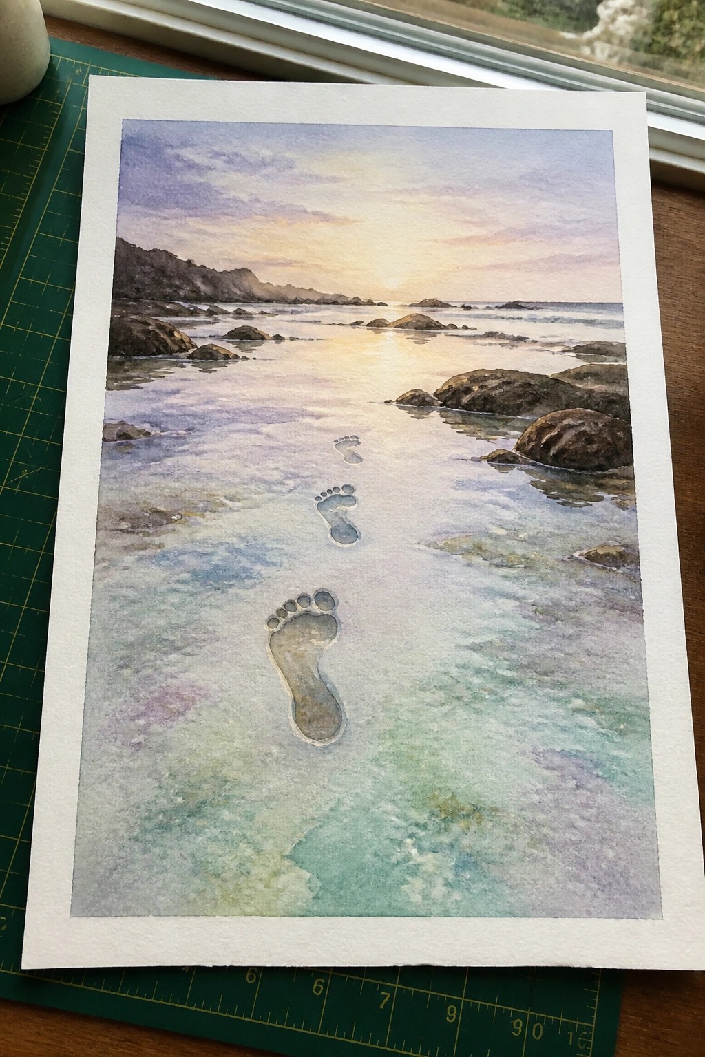 Watercolor painting of footprints in shallow turquoise water on rocky beach at sunset