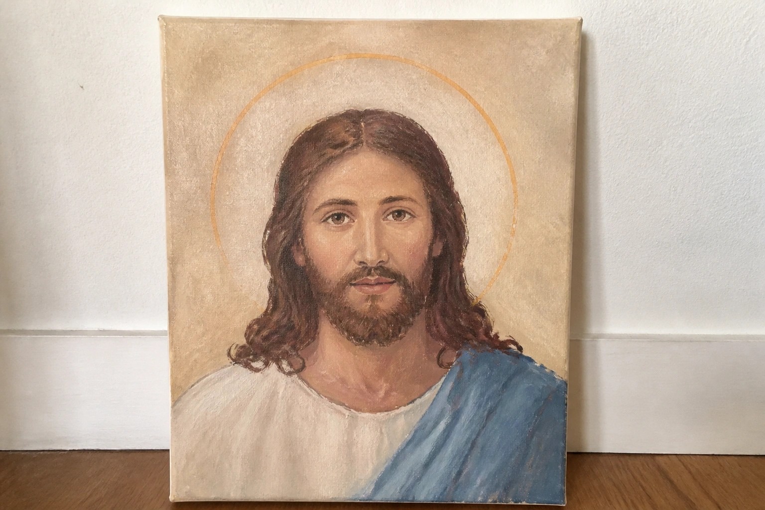 Canvas painting of Jesus with halo and robes propped on wooden floor against wall