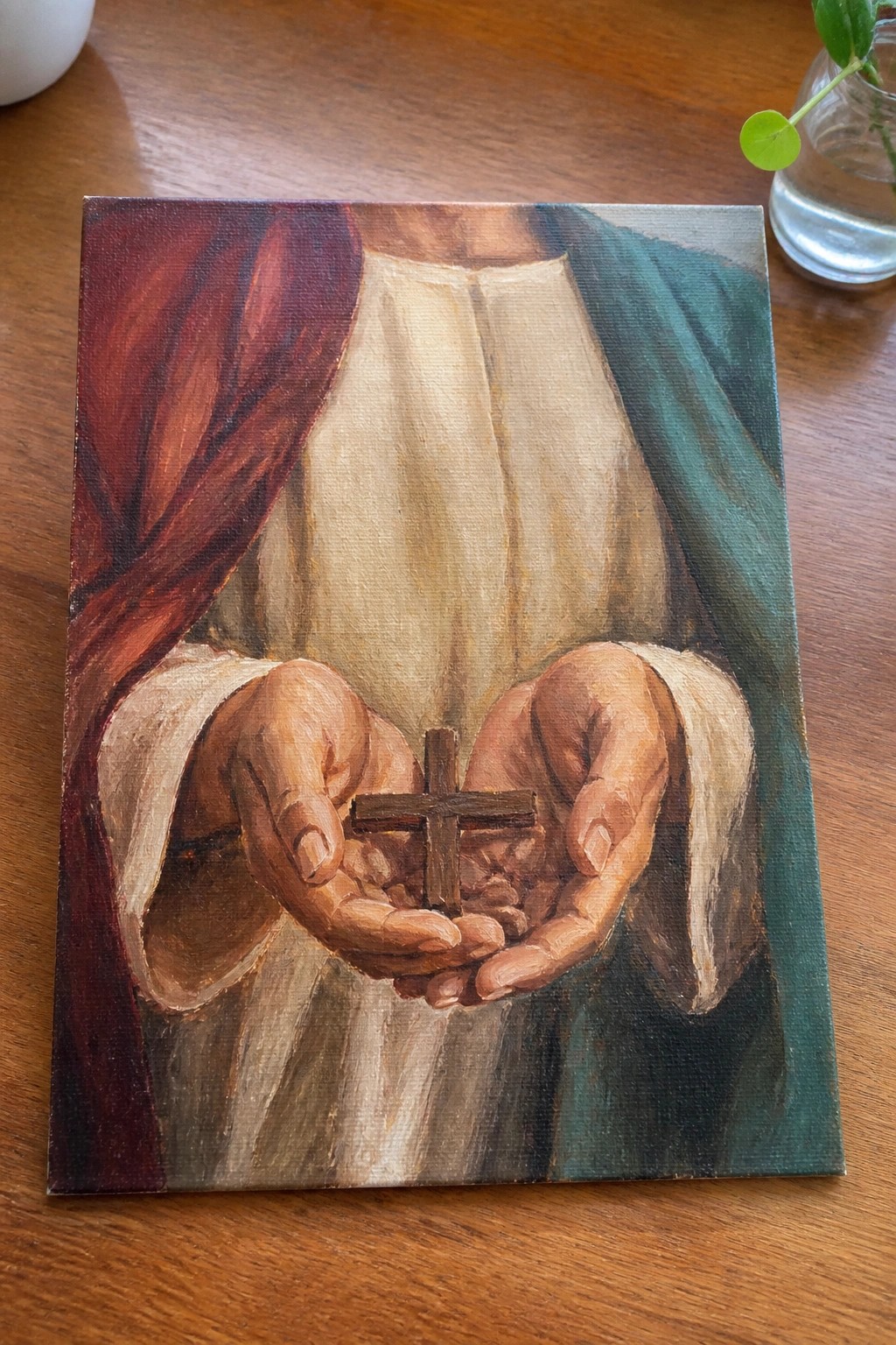 Hands in red, white, and green robes holding a small wooden cross.