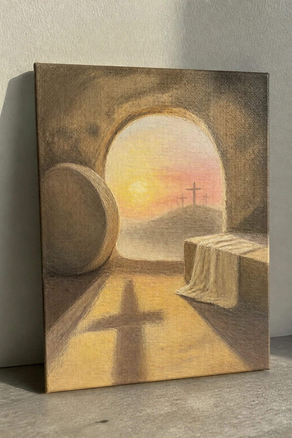 Tomb interior with rolled stone, cloth-draped slab, cross shadow, and sunrise over three crosses.
