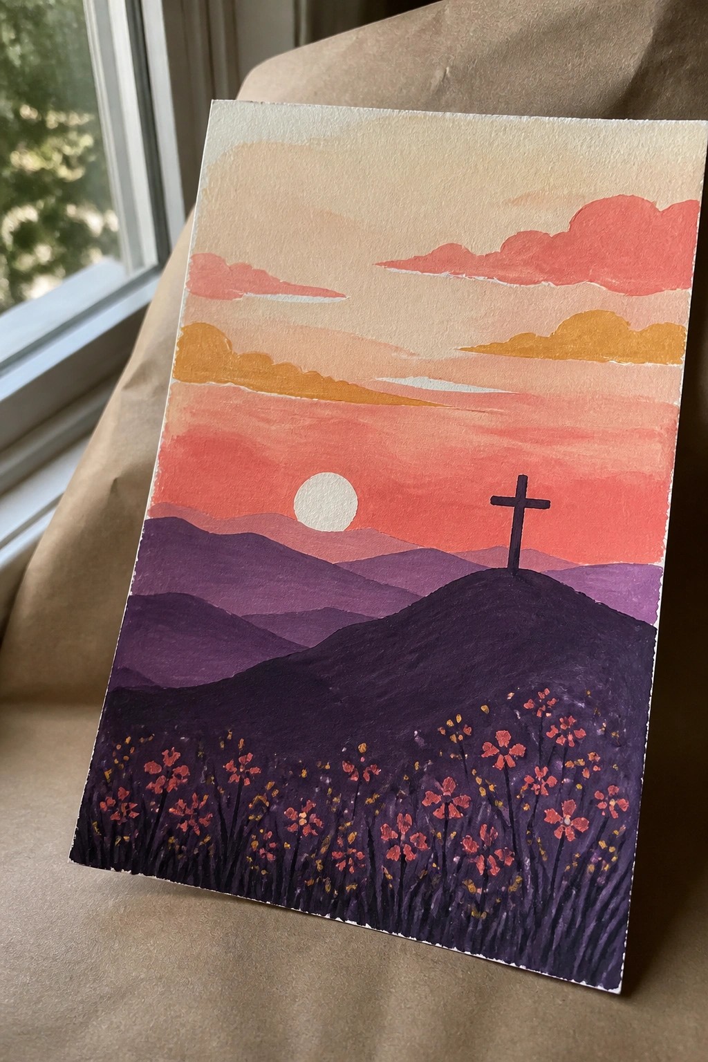 Watercolor sunset landscape with cross on purple hill, orange sky, and red wildflowers.